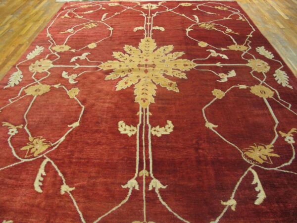 Red rug with a golden central medallion and scrolling cream floral patterns on a wood floor.