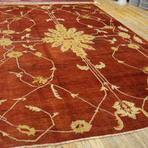 Terracotta rug featuring a large, light gold botanical pattern on rustic wooden floors.