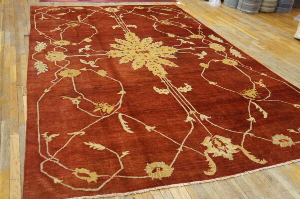 Terracotta rug featuring a large, light gold botanical pattern on rustic wooden floors.