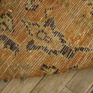 The tightly woven rug features rust, olive, and dark brown geometric patterns laid on light wood planks.