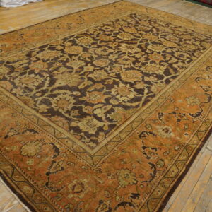 Distressed floral rug featuring dark brown and terracotta colors displayed on worn wooden plank flooring.