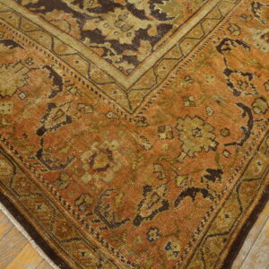 Low-pile rug in rust and dark green traditional patterns rests on distressed blonde wood flooring.