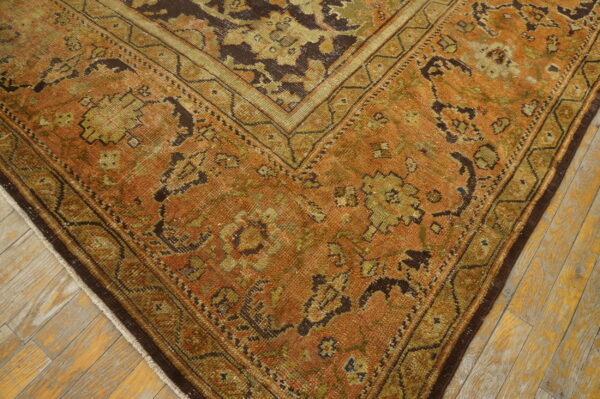 Low-pile rug in rust and dark green traditional patterns rests on distressed blonde wood flooring.