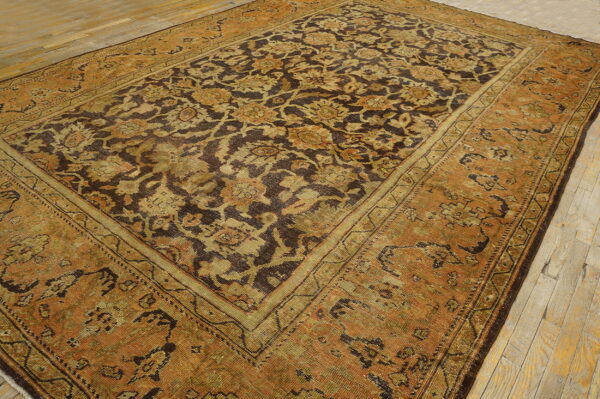 Rust-toned rug with a dense dark brown and olive green floral pattern on distressed wood flooring.
