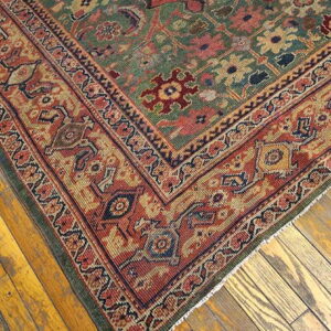 Traditional rug corner featuring a muted green field and wide rust border on distressed hardwood floors.
