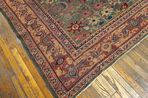 Traditional rug corner featuring a muted green field and wide rust border on distressed hardwood floors.