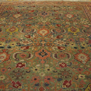 Low-pile rug with a dense traditional floral pattern in green, rust, and yellow on wood plank flooring.