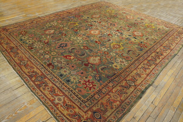 Large traditional rug with a detailed green and rust floral pattern visible on rustic plank flooring.