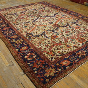Large cream and rust floral rug with a contrasting navy border rests on rustic hardwood plank flooring.