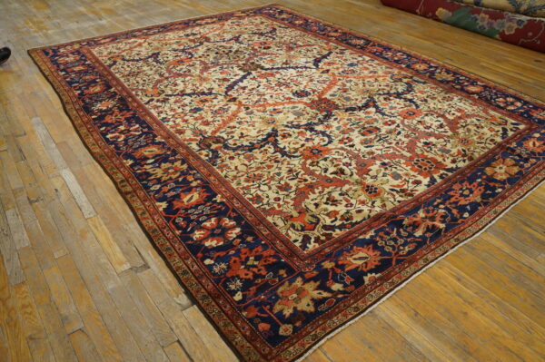 Large cream and rust floral rug with a contrasting navy border rests on rustic hardwood plank flooring.