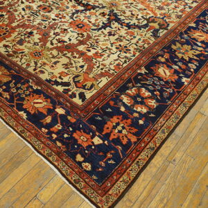 Floral rug corner with cream, rust, and navy colors laid on worn light brown plank wood flooring.