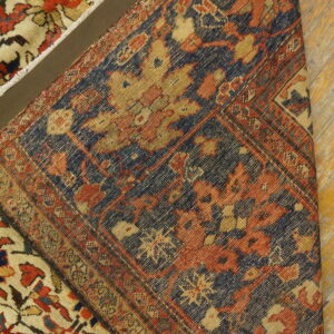 A tightly patterned navy and rust rug section is folded over a cream and red floral patterned rug on wood flooring.