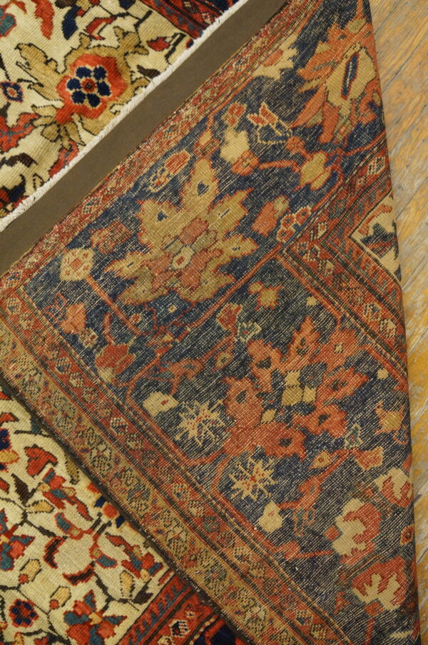 A tightly patterned navy and rust rug section is folded over a cream and red floral patterned rug on wood flooring.