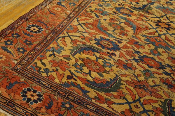Gold and orange traditional rug with complex blue floral patterns resting on light hardwood flooring.