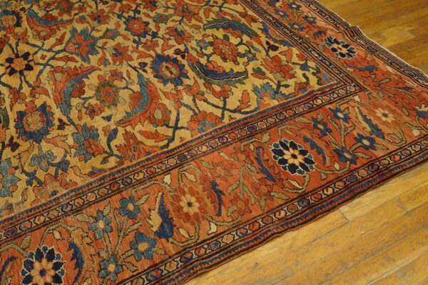 Gold, rust, and navy traditional rug showing dense floral patterns and a wide border on wood planks.