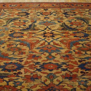 Intricate floral rug featuring a golden field with rust and blue patterns on wood flooring.