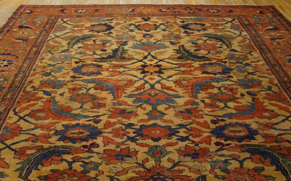 Intricate floral rug featuring a golden field with rust and blue patterns on wood flooring.