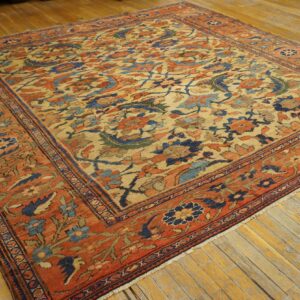 Traditional tan rug with dense rust, navy, and blue floral motifs rests on worn wood flooring.