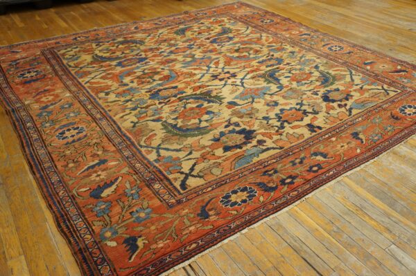 Traditional tan rug with dense rust, navy, and blue floral motifs rests on worn wood flooring.