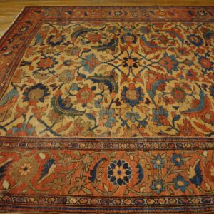 Ornate traditional rug in muted gold, deep blue, and rust colors rests on distressed light wood flooring.