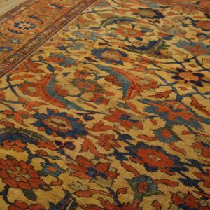 Low-pile rug with complex floral design in red, blue, and gold on wooden plank flooring.