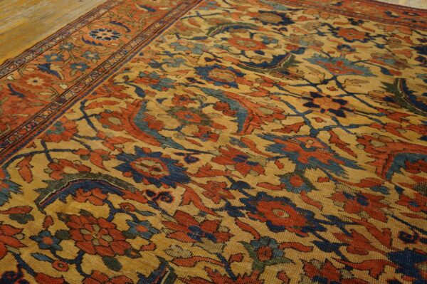 Low-pile rug with complex floral design in red, blue, and gold on wooden plank flooring.