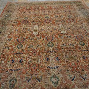 Worn rust and muted green traditional rug with intricate patterns lies on light, distressed wood plank flooring.