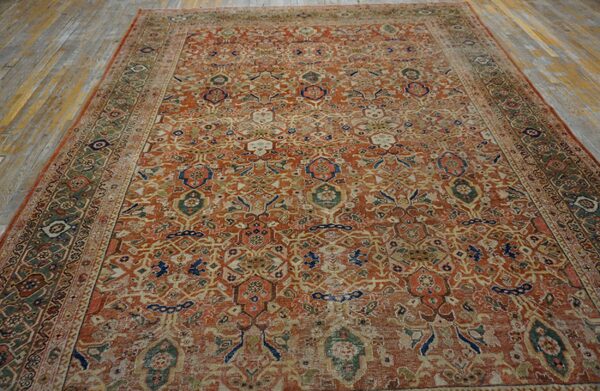 Worn rust and muted green traditional rug with intricate patterns lies on light, distressed wood plank flooring.