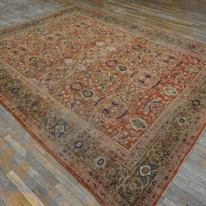 Rust and green traditional patterned rug with a wide border displayed on gray wooden floorboards.