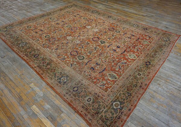 Rust and green traditional patterned rug with a wide border displayed on gray wooden floorboards.