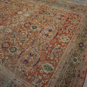 Ornate distressed rug featuring rust orange, sage green, and blue patterns on aged gray wood flooring.