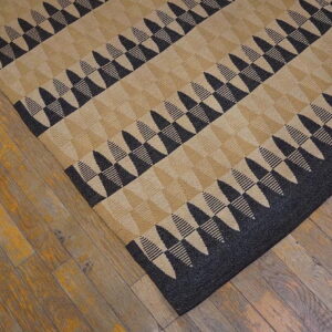 Black and tan rug with a zigzag triangular pattern cornered on distressed brown wood flooring.