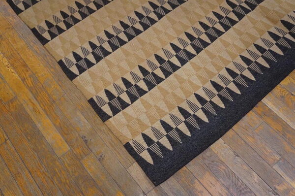 Black and tan rug with a zigzag triangular pattern cornered on distressed brown wood flooring.