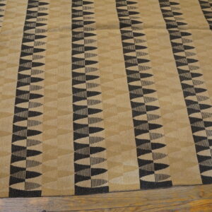 Tan and dark geometric rug with serrated vertical stripes lays on exposed wood flooring.