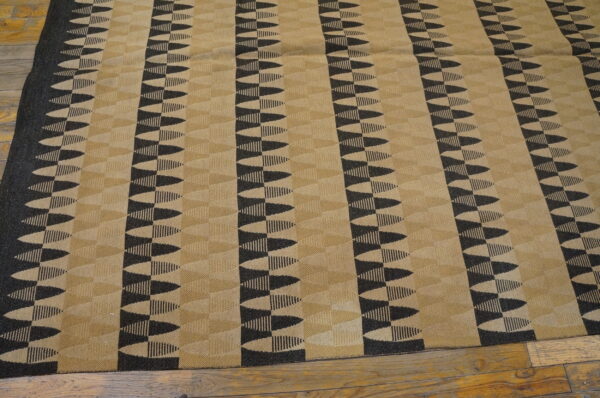 Tan and dark geometric rug with serrated vertical stripes lays on exposed wood flooring.