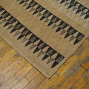 Low-pile tan rug with black geometric triangles and stripes visible on rustic hardwood flooring.