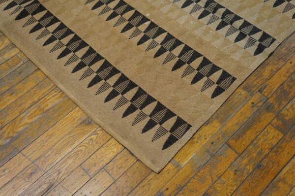 Low-pile tan rug with black geometric triangles and stripes visible on rustic hardwood flooring.
