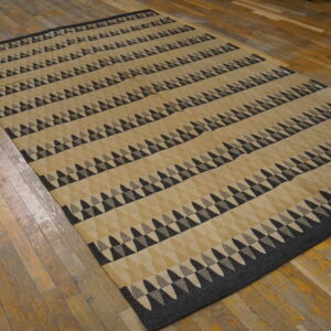 Low pile tan rug with horizontal bands of black and gray geometric triangles on worn wood planks.