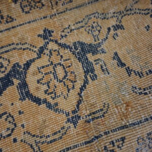 Textured close-up of a gold and navy rug featuring a geometric pattern and visible low, ribbed pile.