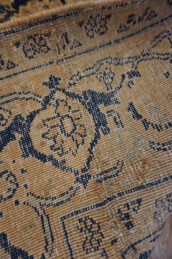 Textured close-up of a gold and navy rug featuring a geometric pattern and visible low, ribbed pile.