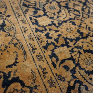Detail of a low pile rug featuring an elaborate navy blue pattern on a golden brown background.