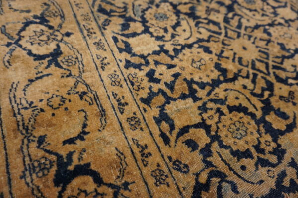 Detail of a low pile rug featuring an elaborate navy blue pattern on a golden brown background.