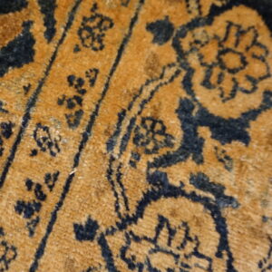 Extreme close-up of a low-pile rug featuring dark blue floral motifs on a gold field.