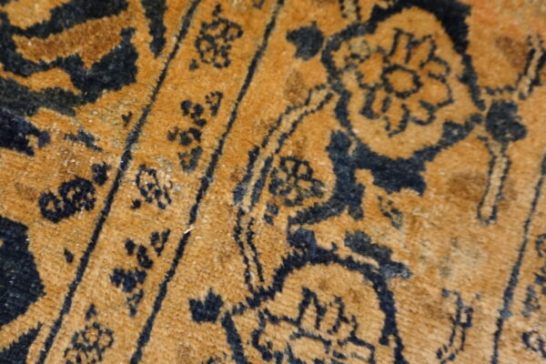 Extreme close-up of a low-pile rug featuring dark blue floral motifs on a gold field.