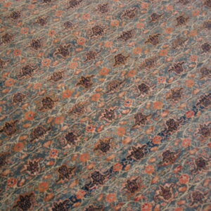 Muted teal rug detail featuring diagonal rows of dark floral and peach colored blossom patterns.