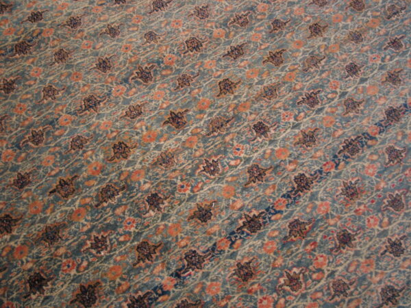 Muted teal rug detail featuring diagonal rows of dark floral and peach colored blossom patterns.