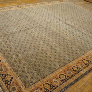 Muted sage rug with dense geometric field and wide rust and navy floral border on distressed wood floor.