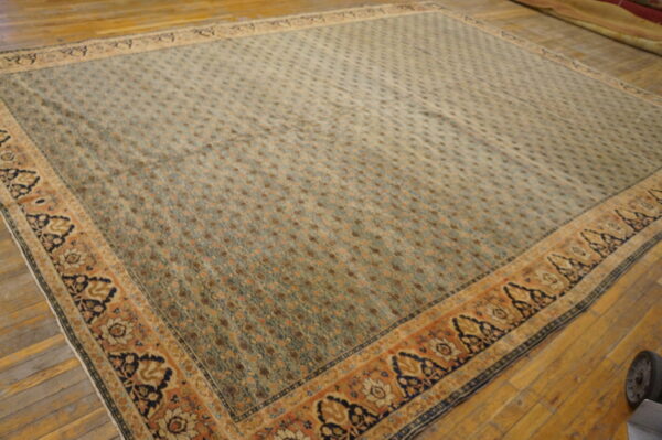 Muted sage rug with dense geometric field and wide rust and navy floral border on distressed wood floor.