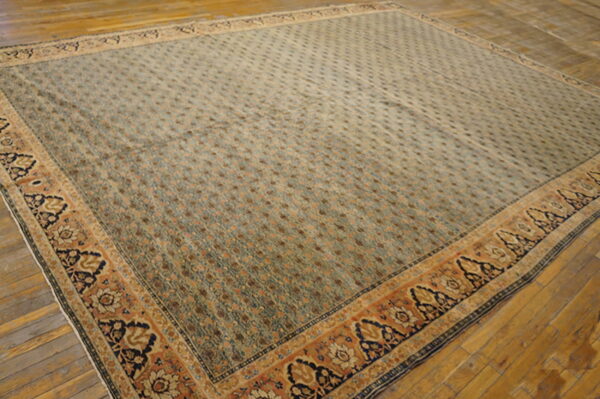 Large square rug with a dense sage and brown field pattern, framed by a wide rust and navy floral border on a wood floor.
