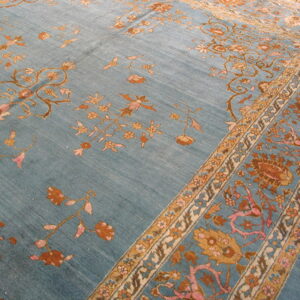 Close-up of a blue rug with intricate floral patterns in rust, gold, and pink, resting on hardwood floors.